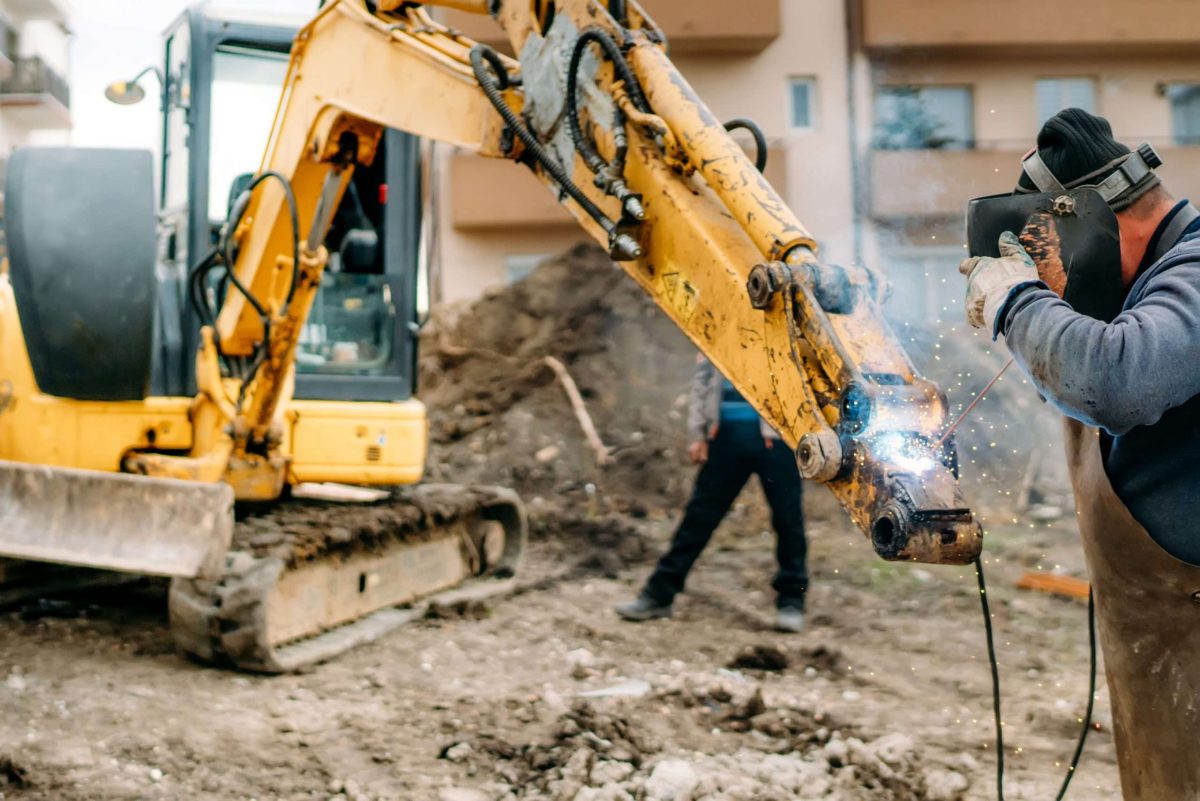 Construction worker welding broken excavator on construction site